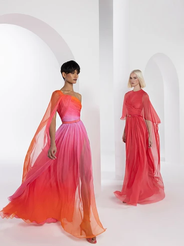 Deux modèles féminins portant des robes longues et fluides en dégradé de rose et orange, posant dans un studio blanc moderne avec des arches en arrière-plan