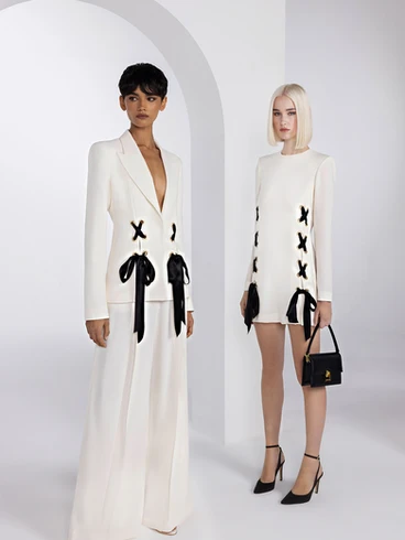 Deux modèles féminins portant des tenues blanches élégantes avec des détails noirs, l'une en robe longue avec décolleté plongeant et l'autre en mini-robe, posant dans un studio blanc avec une arche