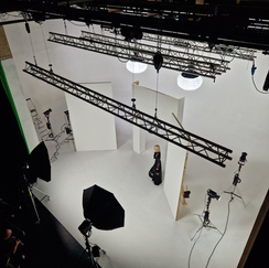 Vue aérienne d'un grand studio de photographie avec une femme posant, entourée de nombreux équipements d'éclairage, caméras, et une structure de support métallique au plafond